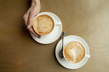 Two cups of cappuccino with latte art in white cups on wooden table. Morning coffee for couple in love. Top view. 