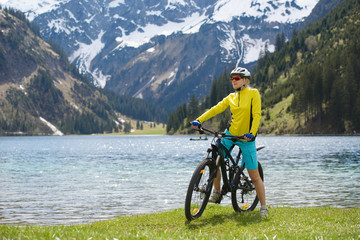 Obraz premium Young woman riding a bike on the lake in a beautiful mountain landscape