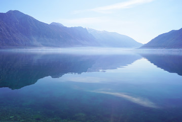 Morning landscape in blue color from Boka Bay, Montenegro: high mountains and their exact reflection in the sea water.