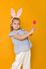 Portrait of cute little child girl with Easter bunny ears holding colorful eggs on yellow background. Happy easter