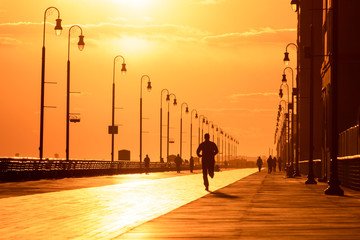 Silhouette of a person running on a boardwalk at sunset. People enjoying outdoor activities under...