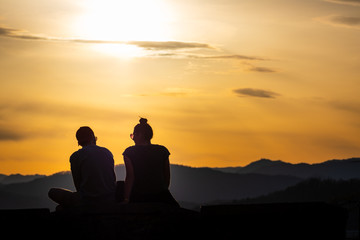 Fototapeta na wymiar Teenager couple with sunglasses sitting on hill enjoying the sunset