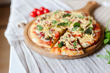 Homemade italian pizza, fresh cherry tomatoes and basil, arugula served on wooden board on kitchen table with linen towel.