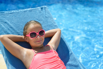 Beautiful little girl with sunglasses relaxing at the swimming pool