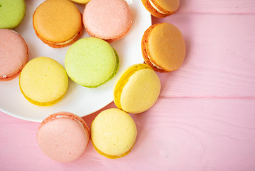 Colorful French or Italian macarons stack on white plate put on pink wood table with copy space for background. Dessert for served with afternoon tea or coffee break.