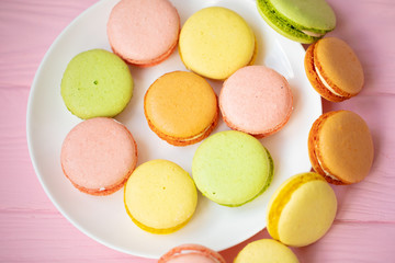 Colorful French or Italian macarons stack on white plate put on pink wood table with copy space for background. Dessert for served with afternoon tea or coffee break.