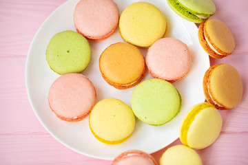 Colorful French or Italian macarons stack on white plate put on pink wood table with copy space for background. Dessert for served with afternoon tea or coffee break.