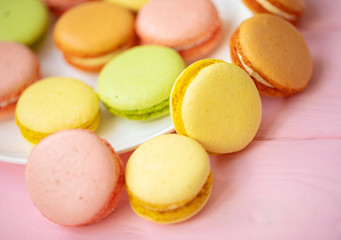 Colorful French or Italian macarons stack on white plate put on pink wood table with copy space for background. Dessert for served with afternoon tea or coffee break.