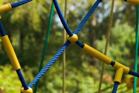 Detail of rope climbing frame  for children.Blue, green and yellow ropes with yellow plastic clutchs. Detail of climbing frame