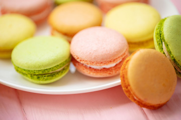 Colorful French or Italian macarons stack on white plate put on pink wood table with copy space for background. Dessert for served with afternoon tea or coffee break.