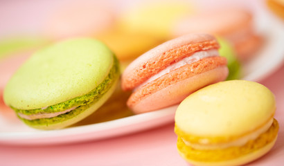Colorful French or Italian macarons stack on white plate put on pink wood table with copy space for background. Dessert for served with afternoon tea or coffee break.