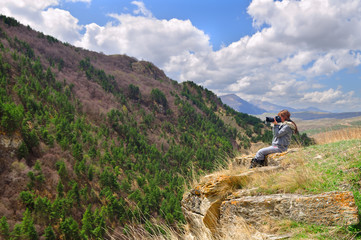 Obraz premium Girl sitting on the edge of a cliff and taking pictures of the mountain landscape