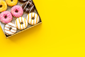 Glazed decorated donuts in box for sweet break on yellow background flat lay copy space