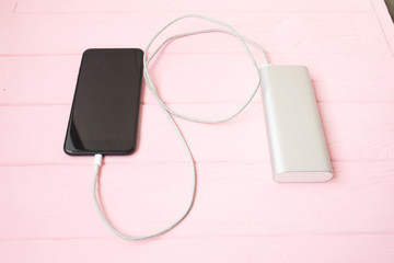 Phone charging with energy bank. Depth of field on Power bank. Pink wooden background.