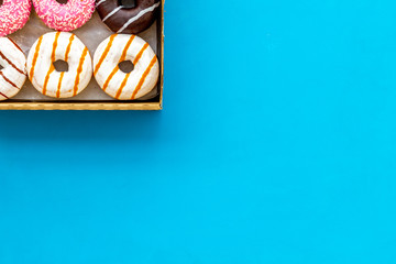 Glazed decorated donuts in box for sweet break on blue background flat lay copy space