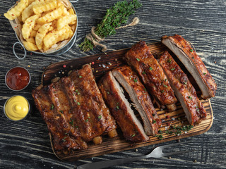 cutting grilled pork ribs with sauce on a board, french fries, spices, wooden background