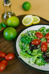Fresh salad from different kinds of greens and a cherry tomato, dressed with olive oil and sprinkled with sesame seeds.