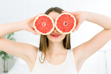 Pretty young girl with grapefruit slices in front of her eyes. Beautiful woman holding grapefruit slice hiding eyes behind isolated on white background
