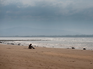 Woman siting on a beach, concept relaxing listening to oceans wave noise. Silverstrand beach, Ireland. Peacefull and relaxing atmosheare.
