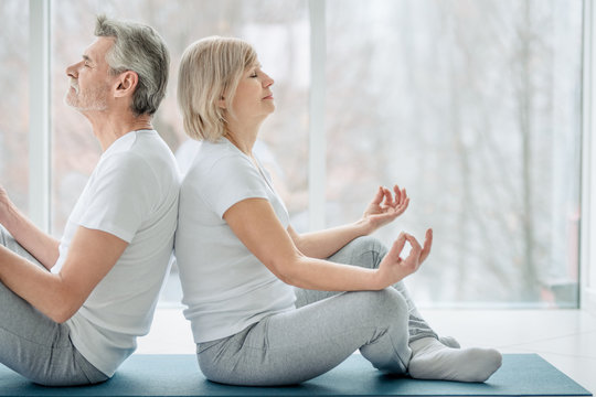 Meditation together.Cropped picture of senior couple doing yoga together in the white gym. Health and sport concept.
