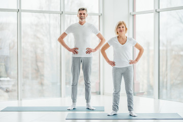 Ready to start training. Beautiful elderly couple standing in a spacious white fitness room before a sport session.