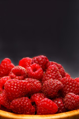 Photo of raspberries in wooden cup on black background