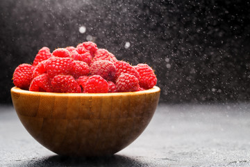 Photo of raspberries in wooden cup on black background