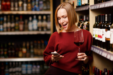 Photo of blonde with phone and glass in hands at store with wine