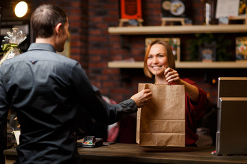 Photo of girl seller with paper bag and man shopper from back
