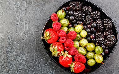 Photo on top of blackberries, strawberries, raspberries, gooseberries,black currant on black plate