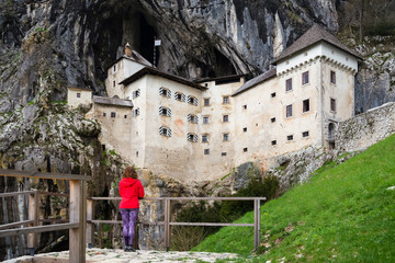 Young woman is admiring the magnificent Predjama Castle which is one of the most famous landmarks in Slovenia, attracting  thousands of tourists each year.