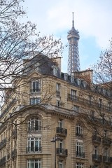 Fototapeta premium Paris, façade d'immeuble haussmannien et vue sur le sommet de la tour Eiffel (France)