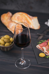 Glass of red wine with slices of cured ham or Spanish jamon serrano or Italian prosciutto crudo, bread, green olives and arugula