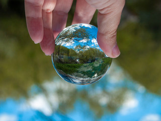 An unrecognizable person with a crystal ball in his hand with a landscape reflection