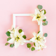 Floral frame made of white lilies and eucalyptus leaves on pink background. Flat lay, top view floral mockup with empty space for text. Floral pattern.