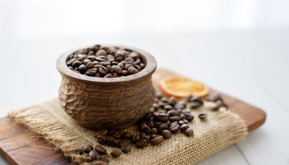 Closeup of coffee beans in wooden rustic bowl on bright background decorated with orange slice.