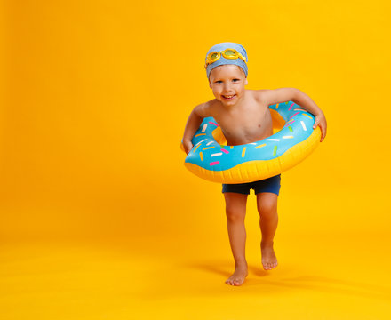 happy child boy in swimsuit with swimming ring donut on colored yellow background.