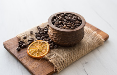 Closeup of coffee beans in wooden rustic bowl on bright background decorated with orange slice.