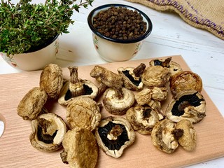 Dried mushrooms on cutting board on white wooden kitchen table with thyme and black peppercorns