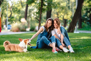 Two female friend in the park play with little dog