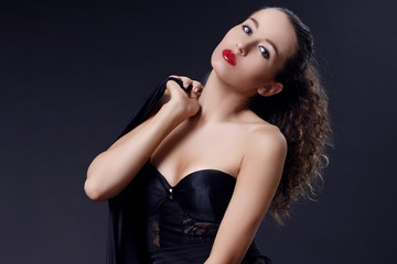 Naklejka premium Portrait of beautiful young girl in a silk black dress with lace corsage on dark background. Elegant woman in a black dress on a dark background