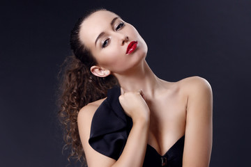 Naklejka premium Portrait of beautiful young girl in a silk black dress with lace corsage on dark background. Elegant woman in a black dress on a dark background