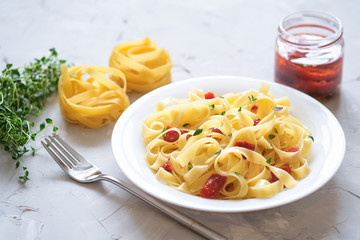 Italian traditional pasta tagliatelle with dried tomatoes and thyme on a light background.