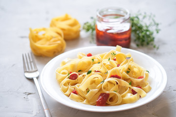 Italian traditional pasta tagliatelle with dried tomatoes and thyme on a light background.