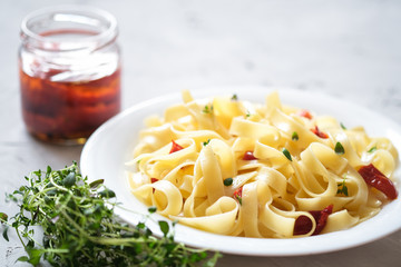Italian traditional pasta tagliatelle with dried tomatoes and thyme on a light background.