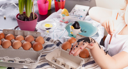 Little girl paints eggs for Easter in the kitchen at home. Child and holiday items of spring. A happy child draws. Copy space.