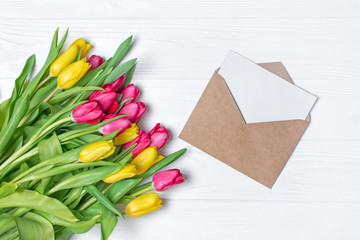 Top view on yellow and pink tulips bouquet with mockup of greeting card in kraft envelope