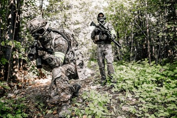 Armed soldiers in camouflage with sniper rifles walking along the path in the dense forest...
