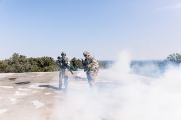 Army soldiers during military operation standing with sniper rifles in smoke. Concept of war, army...