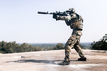 Armed man in camouflage with sniper gun in hand standing on the roof